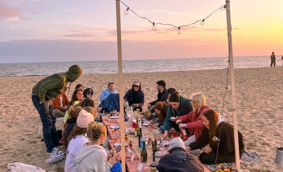 Grupo de amigos jantando na praia ao pôr do sol