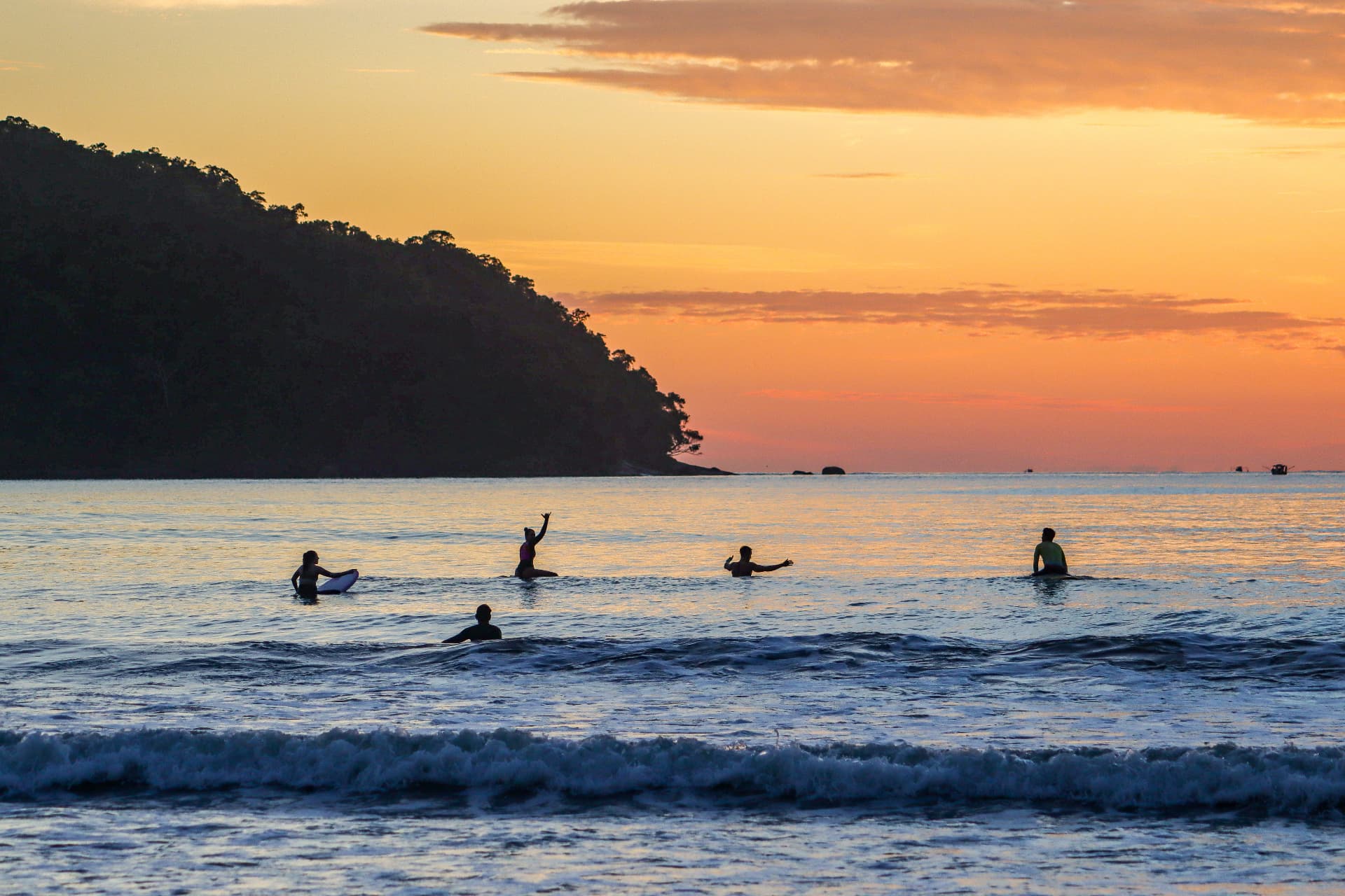 Silhuetas do grupo com pranchas no mar ao pôr do sol em Ubatuba