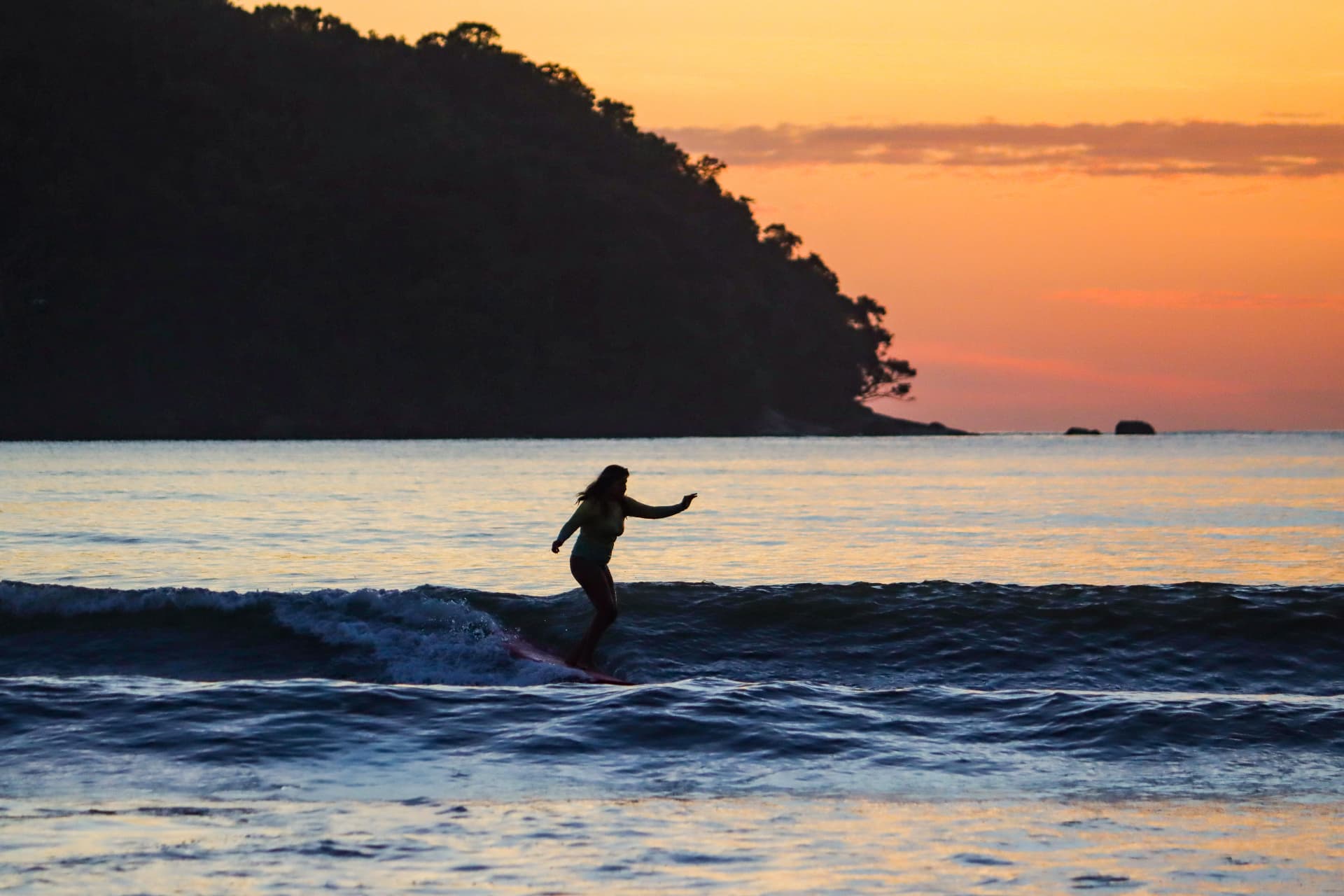 Aluna pegando uma onda ao pôr do sol em Ubatuba